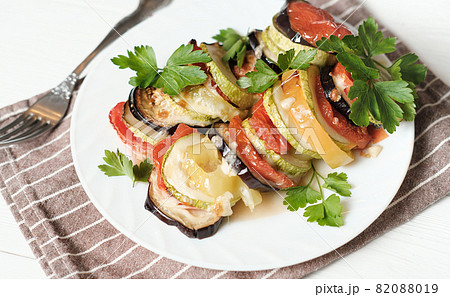 baked vegetables with cheese and parsley on a white plate, home dinner idea. vegetarian menu. sliced and roasted eggplants, tomatoes and zucchini. baked vegetables with cheese and parsley on a white plate, home dinner idea. vegetarian menu. sliced and roasted eggplants, tomatoes and zucchini. 82088019