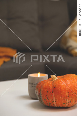Pumpkin and Concrete candlestick on table in living room next to sofa with pillows and blanket. Autumn comfort hyggelig at home 82090077