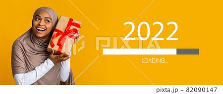 Black Muslim woman in hijab guessing what is inside gift box, waiting for New Year 2022, collage with loading bar 82090147