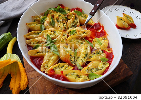 Big shell shape pasta stuffed with creamy soft cheese, zucchini and spinach sprinkled with parmesan cheese in baking dish wooden table, healthy dinner recipe, view flat lay . 82091004