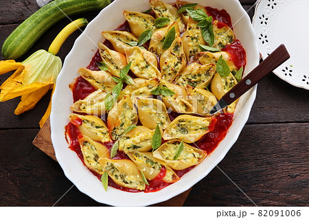 Big shell shape pasta stuffed with creamy soft cheese, zucchini and spinach sprinkled with parmesan cheese in baking dish wooden table, healthy dinner recipe, view flat lay . 82091006