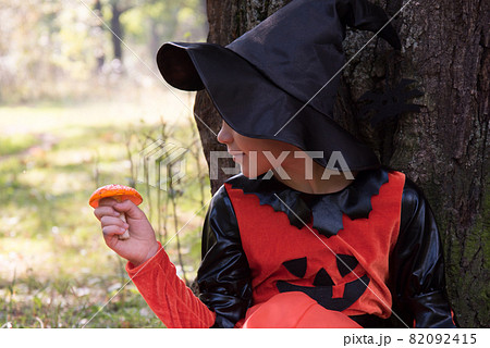 Portrait of a witch. A girl dressed as a witch holds an amanita in her hand. A mushroom for a witch's potion. Beautiful stylish picture in the forest Portrait of a witch. A girl dressed as a witch holds an amanita in her hand. A mushroom for a witch's potion. Beautiful stylish picture in the forest 82092415
