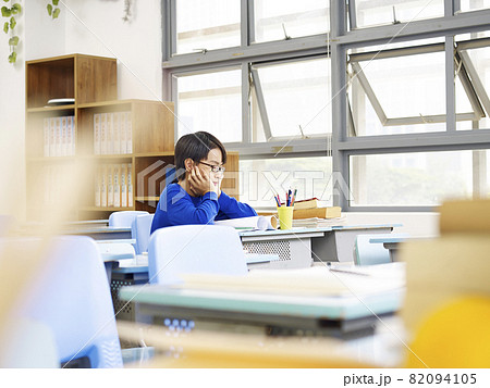 unhappy asian elementary school pupil sitting alone in classroom unhappy asian elementary school pupil sitting alone in classroom 82094105
