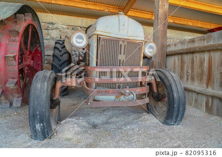 Front of an old and vintage tractor against stone wall and roof of a farm barn 82095316