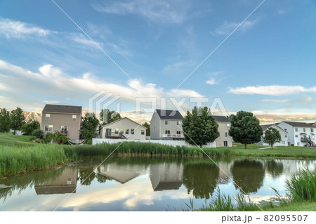 Scenic suburban landscape with homes and cloudy sky reflected on a shiny pond 82095507