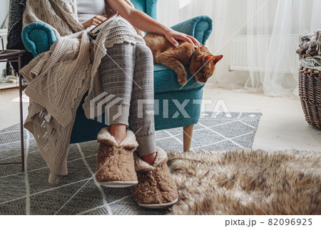 Young woman sitting in a cozy armchair, with a warm blanket, wit 82096925