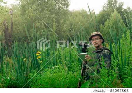 ornithologist with a spotting scope and notepad among the tall grass in the valley ornithologist with a spotting scope and notepad among the tall grass in the valley 82097368