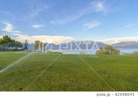 Sprinklers on green grassy field with scenic lake and snowy mountain background Sprinklers on green grassy field with scenic lake and snowy mountain background 82098045