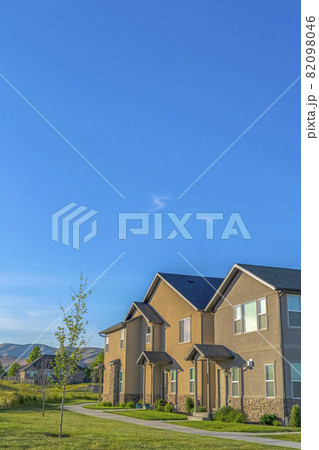 Lush green lawn and pathways in front of homes with porticos against blue sky Lush green lawn and pathways in front of homes with porticos against blue sky 82098046