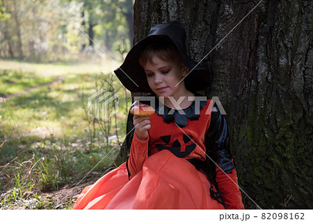 Portrait of a witch. A girl dressed as a witch holds an amanita in her hand. A mushroom for a witch's potion. Beautiful stylish picture in the forest Portrait of a witch. A girl dressed as a witch holds an amanita in her hand. A mushroom for a witch's potion. Beautiful stylish picture in the forest 82098162