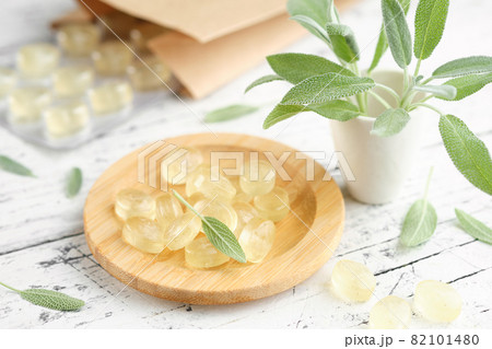 Wooden plate of sage lozengers for care sore throat and cough. Leaves of sage or salvia officinalis plant on white wooden table. Wooden plate of sage lozengers for care sore throat and cough. Leaves of sage or salvia officinalis plant on white wooden table. 82101480