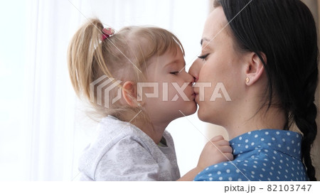 A little girl kisses her beloved mother, mom holds the child in her arms and hugs, the concept of a happy family life, the nanny calms the child, the parent is next to the kid together, 4K, close-up 82103747