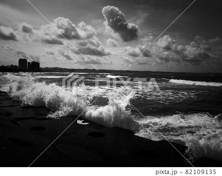 南国の海岸に打ち寄せる波と立体的な雲のモノクロ画像の写真素材