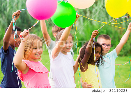 Happy tweens with balloons on green meadow in summer park 82110223