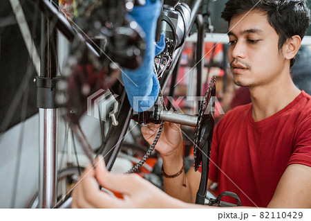 close up of a young man in red working carefully installing bicycle chain 82110429