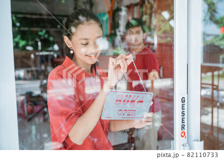 a woman in a red t-shirt prepares to open a shop by posting an open sign on the windshield door 82110733