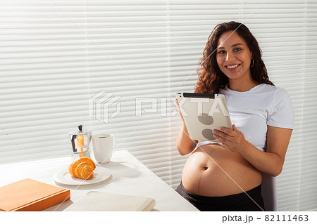 Pregnant woman using digital tablet. Breakfast time. Technology and pregnancy concept. Pregnant woman using digital tablet. Breakfast time. Technology and pregnancy concept. 82111463