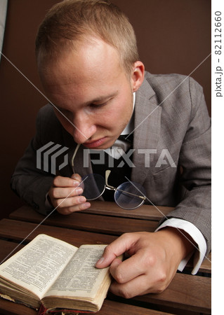 Portrait of a man.A comical, cheerful, cheerful guy in a suit and glasses, holding a book in his hands, carefully examines the book. High quality photo 82112660
