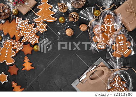A Christmas gingerbread cookie in the shape of a Christmas tree in a cellophane packing on the background of a dark table. Christmas gift concept. 82113380