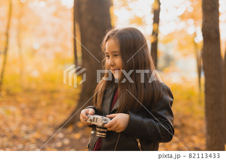 A little girl take a photo with old retro camera in autumn nature. Leisure and hobby concept. 82113433