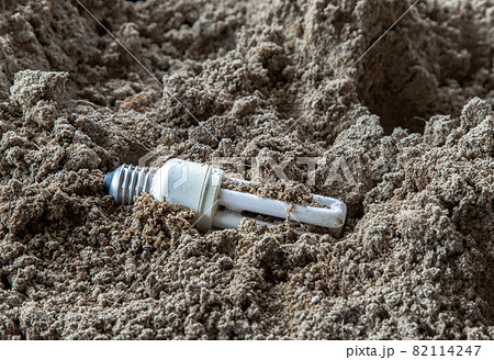 The remains of burnt energy-saving lamp are left on the beach sand. Hazardous and toxic electronic waste. The remains of burnt energy-saving lamp are left on the beach sand. Hazardous and toxic electronic waste. 82114247