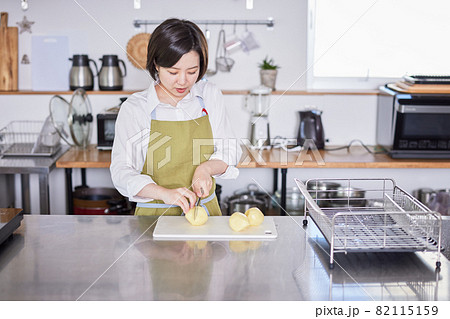 じゃがいもを包丁で切るエプロン姿の若い女性 82115159
