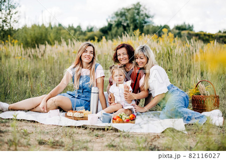 The family is having a picnic on the lawn. Three generations of women of the same family rest together 82116027