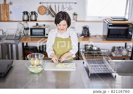 玉ねぎを包丁で切るエプロン姿の若い女性 82116760