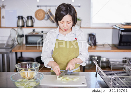 玉ねぎを包丁で切るエプロン姿の若い女性 玉ねぎを包丁で切るエプロン姿の若い女性 82116761