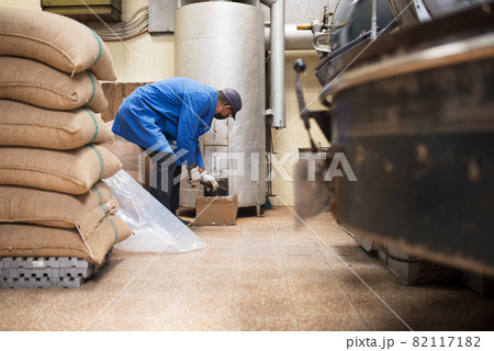 Man in uniform setting up roasting machine 82117182