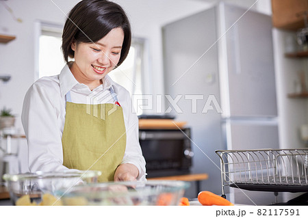 キッチンで料理をするエプロン姿の若い女性 82117591