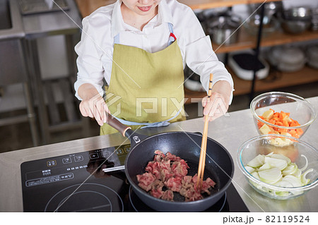 キッチンで牛肉を炒めるエプロン姿の若い女性 82119524