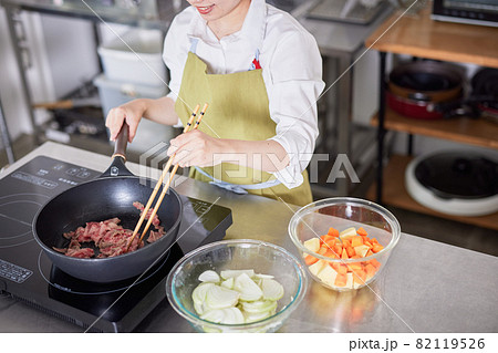 キッチンで牛肉を炒めるエプロン姿の若い女性 キッチンで牛肉を炒めるエプロン姿の若い女性 82119526
