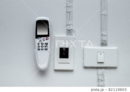 The air conditioner remote is attached to the cement wall and the light switch. The air conditioner remote is attached to the cement wall and the light switch. 82119603