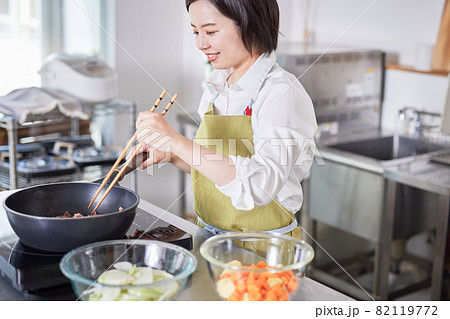 キッチンで料理をするエプロン姿の若い女性 82119772