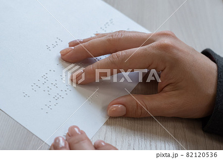 Close-up woman reads the text to the blind. Woman's hands on paper with braille code. Close-up woman reads the text to the blind. Woman's hands on paper with braille code. 82120536
