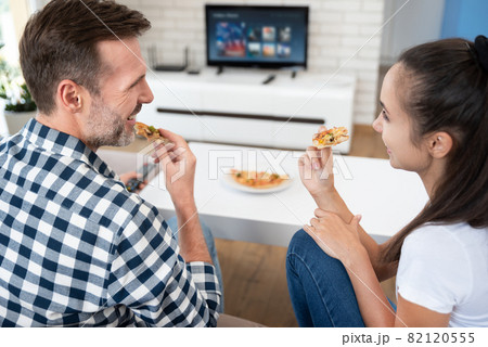 Couple watching TV while eating pizza Couple watching TV while eating pizza 82120555