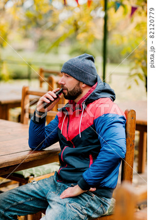 A young man using a mobile phone is sitting outdoors in a cafe or restaurant on an autumn day 82120779