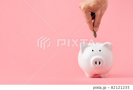 Money saving and investment concept. Hand putting coin to piggy bank on pink background with copy space Money saving and investment concept. Hand putting coin to piggy bank on pink background with copy space 82121235
