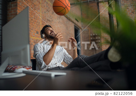 Cheerful young businessman with headphones and ball taking a break in office, resting. 82122056