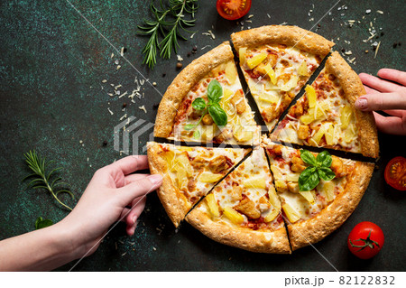 Hot Hawaiian pizza with chicken, pineapple and cheese, hands, taking pieces pizza served with cheese sauce. Delicious traditional Italian pizza on on a dark stone or concrete background. Top view flat Hot Hawaiian pizza with chicken, pineapple and cheese, hands, taking pieces pizza served with cheese sauce. Delicious traditional Italian pizza on on a dark stone or concrete background. Top view flat 82122832