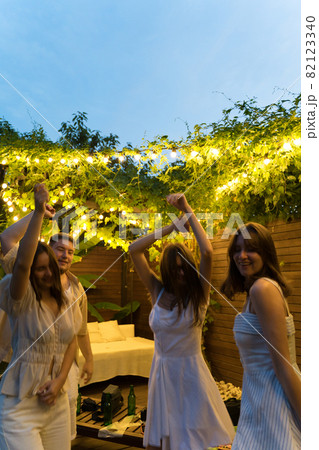 Dancing at a summer party. Fun and joy of friends outside, bottles of beer. A group of people dancing to music in the yard Dancing at a summer party. Fun and joy of friends outside, bottles of beer. A group of people dancing to music in the yard 82123340