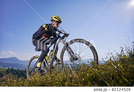 Young man cycling uphill on sunny day with blue sky on background. Male bicyclist in cycling suit climbing uphill on mountain bike. Concept of sport, mountain biking and active leisure. Young man cycling uphill on sunny day with blue sky on background. Male bicyclist in cycling suit climbing uphill on mountain bike. Concept of sport, mountain biking and active leisure. 82124526