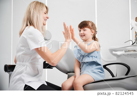 Cheerful girl sitting in dentist chair giving high five to a female dentist after successful visit. Horizontal snapshot, side view. Children's dentistry concept 82124545
