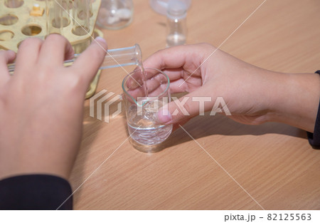Close-up pupil's hands pouring liquid into a beaker. 82125563