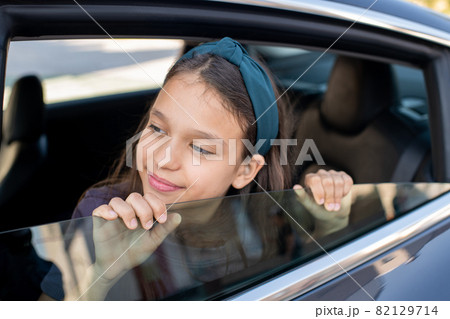 Adorable schoolgirl looking out of window of electric car 82129714