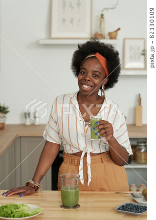 Young cheerful African woman with glass of smoothie Young cheerful African woman with glass of smoothie 82130109