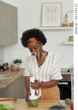 Young female bending over kitchen table while making smoothie 82130111