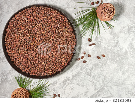 Cedar or pine nuts in a bowl with cones on gray background and a branch of a cedar tree with green needles Cedar or pine nuts in a bowl with cones on gray background and a branch of a cedar tree with green needles 82133093