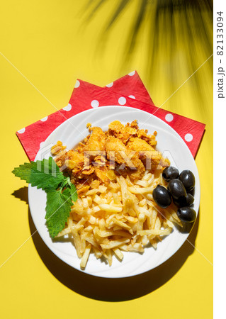 Nuggets with sauce in a plate with French fries and olives on a yellow background with red napkins. hard shadows. Nuggets with sauce in a plate with French fries and olives on a yellow background with red napkins. hard shadows. 82133094